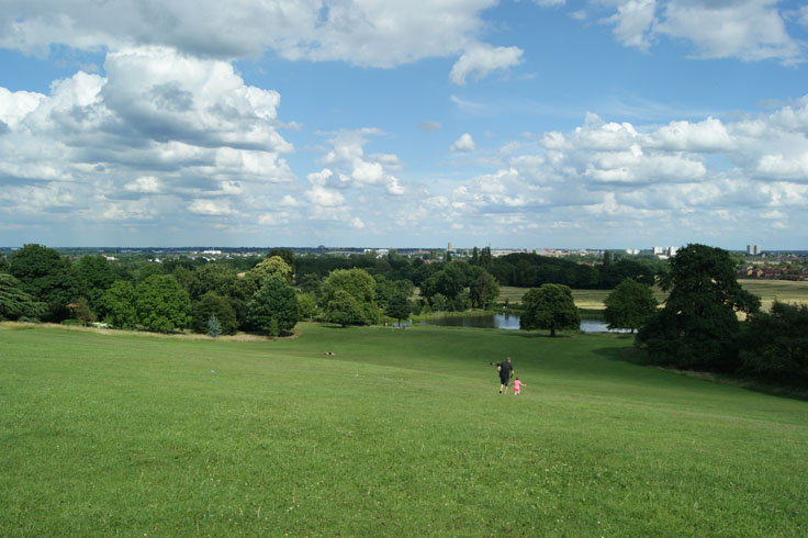 Two people running down a hill towards a lake, with other people sat on the hill. 